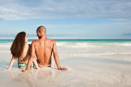 Young mixed-race couple sat on the beach looking out over the sea