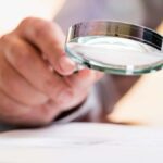 Person holding magnifying glass over important document, reading the small print