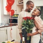 Cropped shot of an affectionate young couple posing with a bunch of flowers in their kitchen on their anniversary