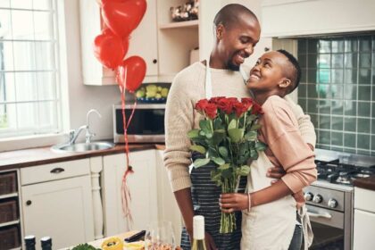 Cropped shot of an affectionate young couple posing with a bunch of flowers in their kitchen on their anniversary