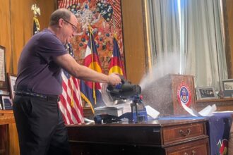 Gov. Jared Polis cuts through executive orders — wielding a circular saw on his desk